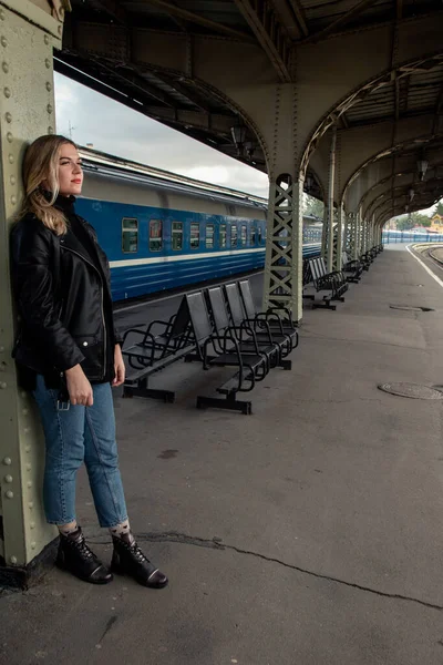Tren istasyonundaki trenin yanında deri ceketli, genç ve güzel bir kadın. St. Petersburg 'daki Vitebsk tren istasyonunu bekliyorum..