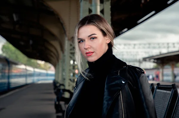 Tren istasyonundaki trenin yanında deri ceketle bankta oturan güzel bir kadının portresi. St. Petersburg 'daki Vitebsk tren istasyonunu bekliyorum..