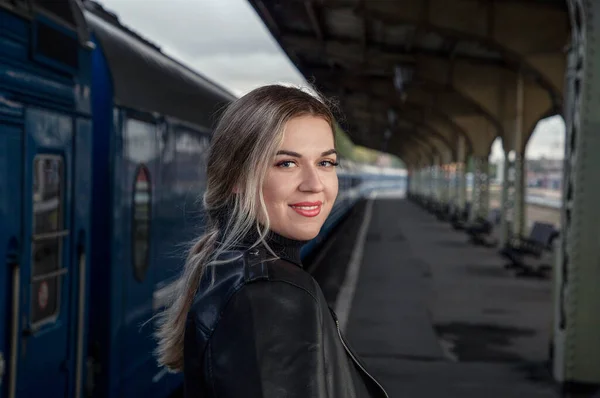 Tren istasyonundaki trenin yanında deri ceketli, güzel bir kadının portresi. St. Petersburg 'daki Vitebsk tren istasyonunu bekliyorum..