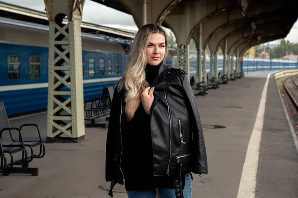 Tren istasyonundaki trenin yanında deri ceketli, güzel bir kadının portresi. St. Petersburg 'daki Vitebsk tren istasyonunu bekliyorum..