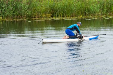 Suzdal, Rusya - 12 Ağustos 2020: Kürek tahtasında adam ve Kamenka nehrinde köpek
