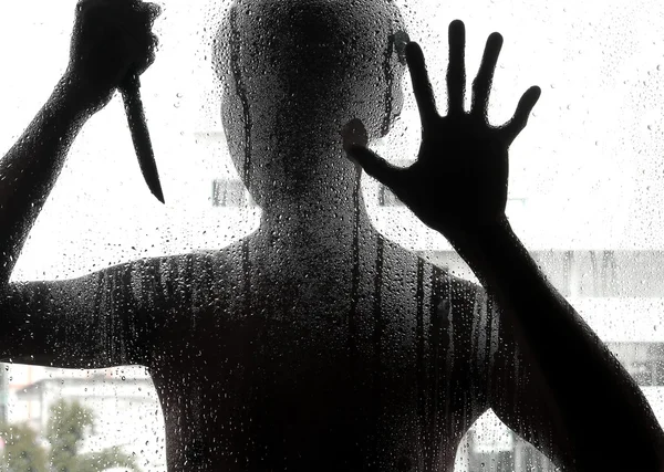Shadowy figure with a knife behind glass — Stock Photo, Image