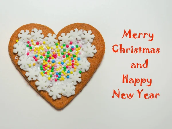 Mutlu Noeller ve mutlu yıllar, el yapımı, kalp şeklinde zencefilli kurabiyenin yanındaki beyaz arka planda renkli şeker süslemeleri olan kırmızı yazı. Tebrik kartı için komik bir tasarım..