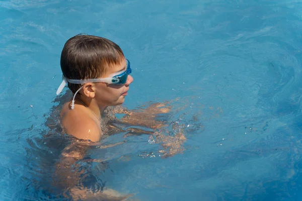 boy in swimming goggles swimming in blue water