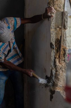 Yaşlı Haitili Latin adam inşaatta çalışıyor duvarı yıkmak için çekiç kullanıyor.