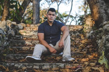 Beyaz tenli erkek modeli Venezuela kökenli Dominik Cumhuriyeti 'nden. Parkta kotlu seksi bir adam, turuncu yürüyüşlü, doğal güneş ışığı olan merdivenlerde oturan.