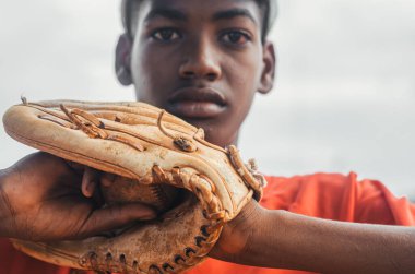 Kahverengi tenli ve latin kökenli çocuk parkta top, eldiven ve sopayla beyzbol oynuyor. Siyah Dominikli çocuk beyzbol üniforması ve şapkası var.