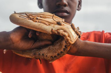 Kahverengi tenli ve latin kökenli çocuk parkta top, eldiven ve sopayla beyzbol oynuyor. Siyah Dominikli çocuk beyzbol üniforması ve şapkası var.