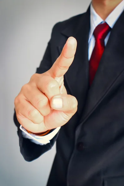 Empresario en traje mostrando gesto apuntan algo sobre fondo gris . — Foto de Stock