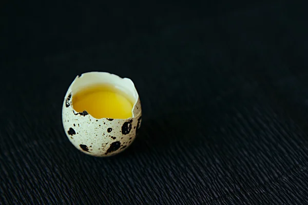 Quail egg on a black textured background. Raw broken egg with the yolk. Easter card. Side view. Background. — Stock Fotó
