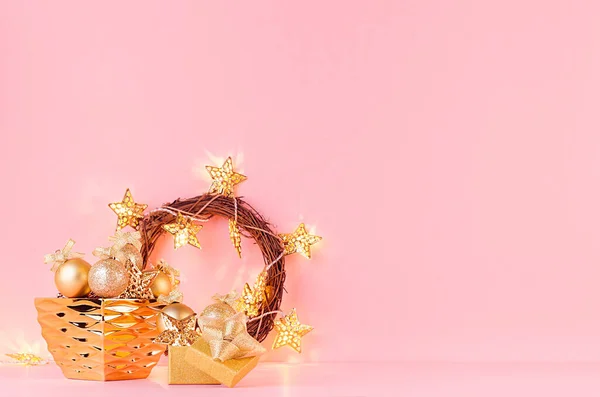 Christmas gold glitter decorations in bowl with christmas wreath, stars garland on soft light pink pastel background with copy space.