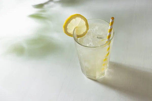 氷のキューブ 葉の緑の影と柔らかい光の白い木のボード上の黄色のレモンスライスを逃したガラスの有機レモンの新鮮なレモンの強壮剤ドリンク — ストック写真