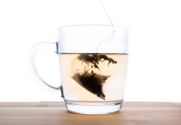 在木桌上的透明杯子里煮了一袋红茶. — 图库照片