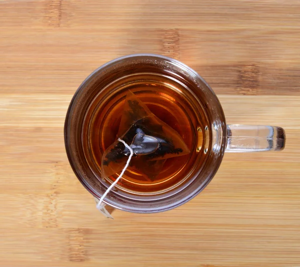 Elaboró una bolsa de té negro en una taza transparente sobre una mesa de madera. —  Fotos de Stock