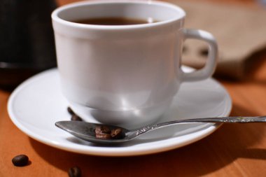 Türk 'ün yanındaki beyaz fincana sade kahve, çuval bezi ve ahşap masaya da tahıl döktü. Boşluğu kopyala.