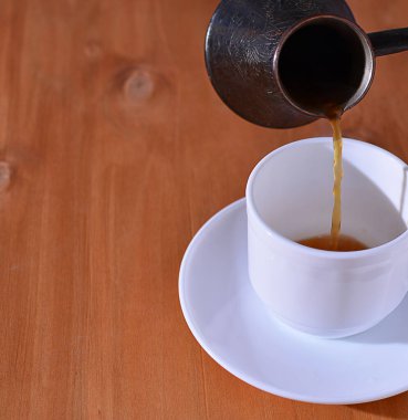 Sıcak kahvenin görüntüsü Türk 'ten beyaz bir fincana dökülüyor, ahşap arka plan. Boşluğu kopyala