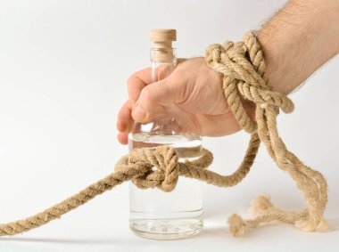 Alkollü cam şişe bir halat düğümüne bağlanır, bir adamın eli şişeyi almaya çalışır, alkolizm tedavisi kavramı, ailede sarhoşluk. Boşluğu kopyala.
