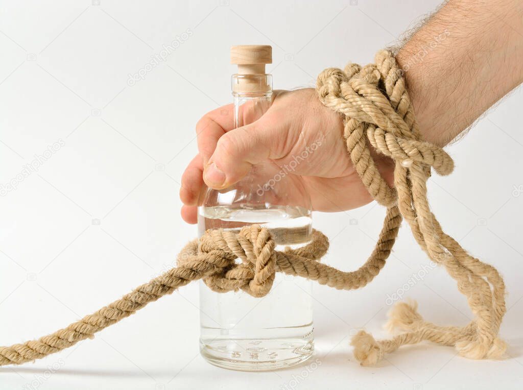 a glass bottle with alcohol is tied in a knot of a rope, a man's hand is trying to take a bottle, the concept of treatment for alcoholism, drunkenness in the family. copy space.