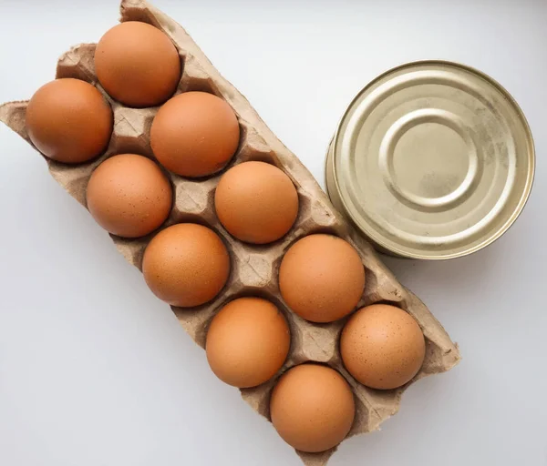 a dozen eggs and a tin of stewed meat on a white background. concept of stocking products for emergency events. top view. flat lay.