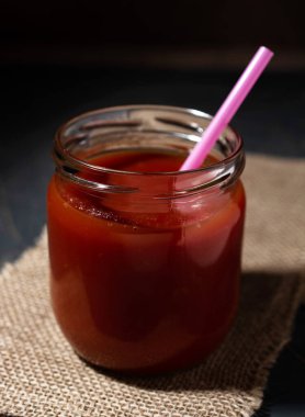 Bir kavanoz domates suyu ve siyah arka planda bir çuval kumaş. Kırsal hayat kavramı, sağlıklı yiyecekler. Boşluğu kopyala.