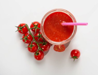 Bardak kavanozunda taze sıkılmış domates suyunun bir kokteyl tüpüyle en üst görüntüsü, yanında beyaz bir masanın arka planındaki bir dalda parlak kırmızı kiraz domatesleri var. kopyalama alanı. düz yat.