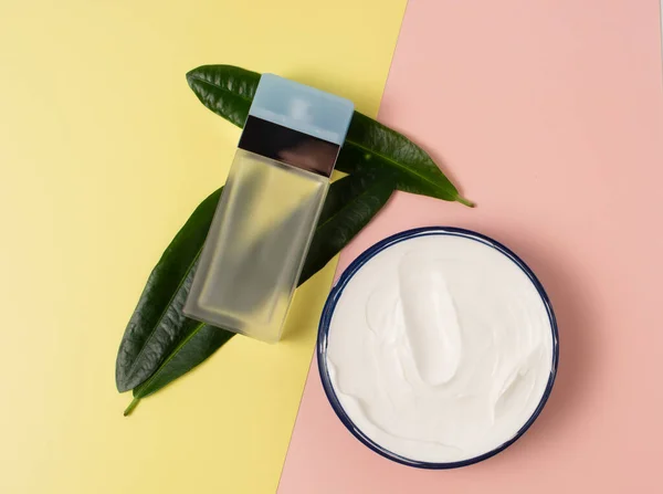 Garrafa de creme cosmético com perfumaria e folhas verdes em um fundo colorido. beleza, relaxamento e rosto e conceito de cuidado do corpo — Fotografia de Stock