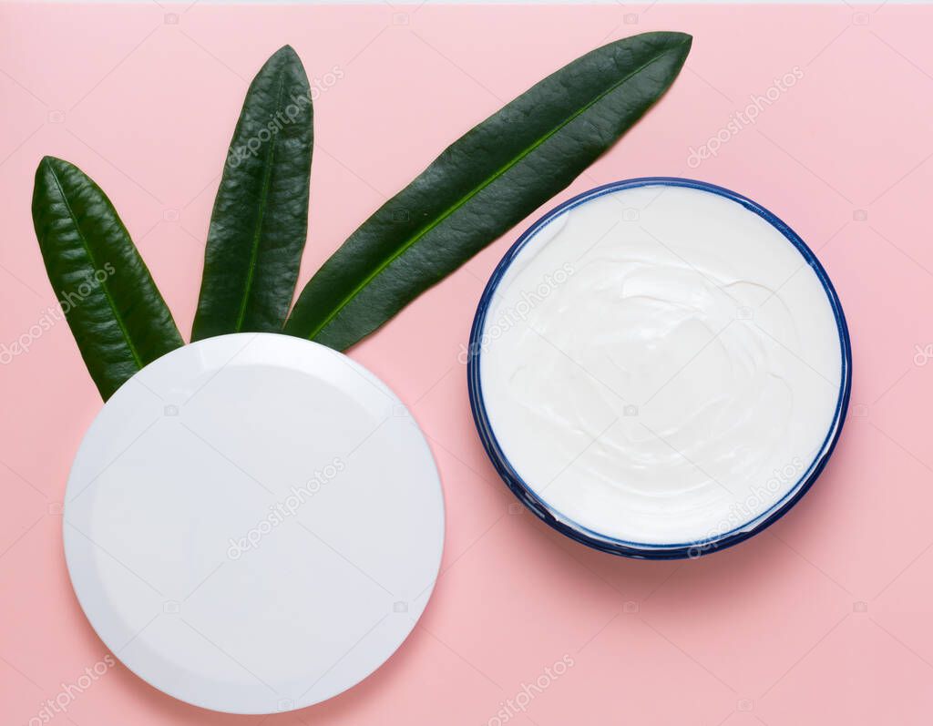 cosmetic cream in a blue jar with white cover and green leaves on a pink background. beauty, relaxation and face and body care concept. flat lay.