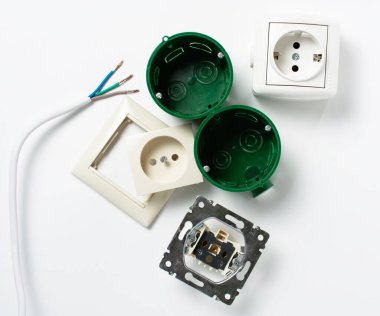 Beyaz bir masada, sökülmüş bir elektrik prizi, sökülmeye hazır, soyulmuş kablolar ve bir elektrikçi için koruyucu eldivenli kırmızı bir tornavida. Elektrik tesisatı, onarım. Boşluğu kopyala.