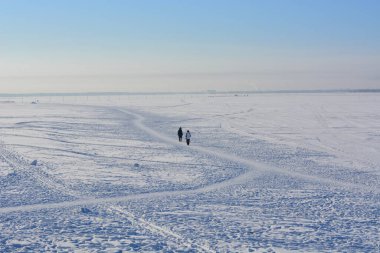 İki kişi donmuş nehrin diğer tarafına geçiyor. Güneşli soğuk bir gün. Kış devam ediyor. Boşluğu kopyala.