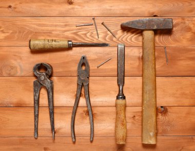 Ahşap bir arka planda eski el aletleri, çekiç, meme ucu, pense, tırnak ve keski kullanılmış..