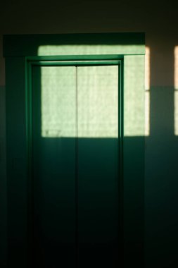 Güneş ışığı pencereden bir apartmanın asansörünün kapısına vuruyor. Boşluğu kopyala.