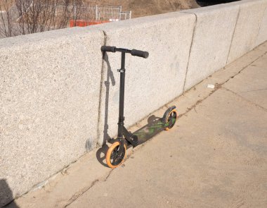 Güneşli bir bahar gününde, granit çitin yanında scooter.