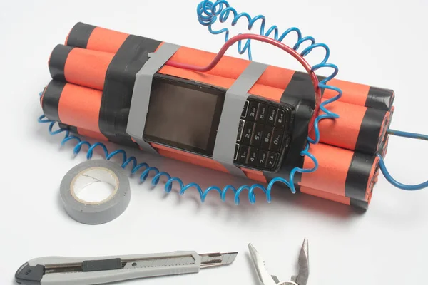 a bomb, a wire tool and an old mobile phone are being assembled on a white table as a timer before the explosion. the concept of terrorism and contract killing. copy space.