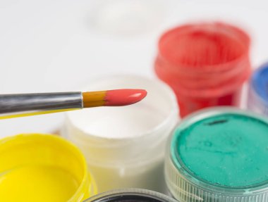 Beyaz arka planda plastik boya kutularının yanında kırmızı boyalı bir fırçanın ucunda. Boşluğu kopyala.