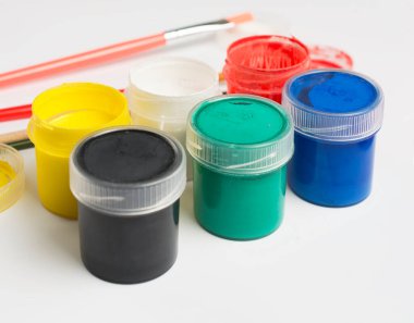 Akrilik boyalı kavanozlar ve beyaz arka planda küçük fırçalar..