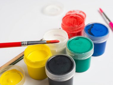 Beyaz arka planda plastik boya kutularının yanında kırmızı boyalı bir fırçanın ucunda. Boşluğu kopyala.