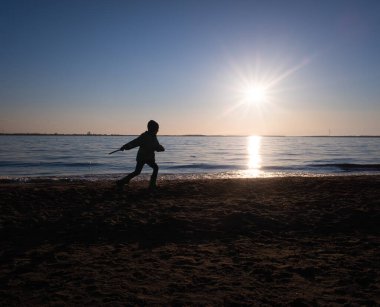 Bir çocuk gün batımında nehre sopa ve taşlar atıyor. Boşluğu kopyala.