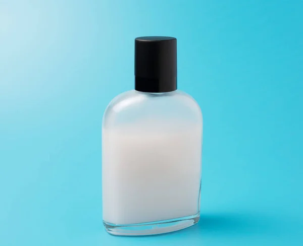 Aftershave lotion i en glasburk med svart skruvlock. isolerad på blå bakgrund — Stockfoto