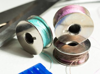 Dikiş makinesi için metal iplik makaraları ve makaslı mavi bir kutuya iğneler. Boşluğu kopyala.