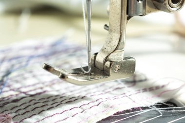Elektrikli dikiş makinesi iğnesiyle mekanizmaya yakın çekim. kumaşın arkaplanına karşı ipliklerle