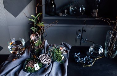 Modern, güzel, koyu renk iç mekan, oda grisi renk, gardırop rafları alışılmadık kasvetli dekorasyon masası kumaşı, kurutulmuş çiçekler, su dolu vazolar, yosun, dallar, alışılmadık bir tarz, cadılar bayramı.