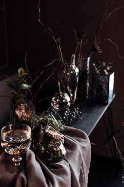 Modern, güzel, koyu renk iç mekan, oda grisi renk, gardırop rafları alışılmadık kasvetli dekorasyon masası kumaşı, kurutulmuş çiçekler, su dolu vazolar, yosun, dallar, alışılmadık bir tarz, cadılar bayramı.