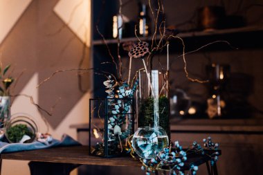 Modern, güzel, koyu renk iç mekan, oda grisi renk, gardırop rafları alışılmadık kasvetli dekorasyon masası kumaşı, kurutulmuş çiçekler, su dolu vazolar, yosun, dallar, alışılmadık bir tarz, cadılar bayramı.