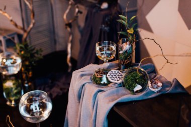 Modern, güzel, koyu renk iç mekan, oda grisi renk, gardırop rafları alışılmadık kasvetli dekorasyon masası kumaşı, kurutulmuş çiçekler, su dolu vazolar, yosun, dallar, alışılmadık bir tarz, cadılar bayramı.