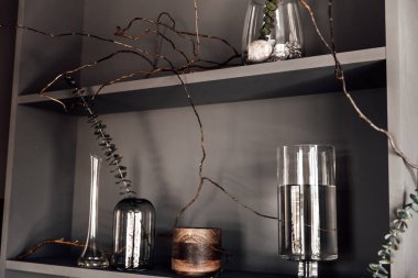 Modern, güzel, koyu renk iç mekan, oda grisi renk, gardırop rafları alışılmadık kasvetli dekorasyon masası kumaşı, kurutulmuş çiçekler, su dolu vazolar, yosun, dallar, alışılmadık bir tarz, cadılar bayramı.