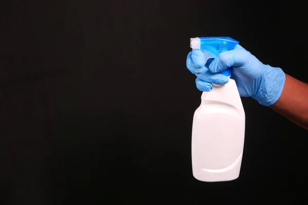 Hand in blue rubber gloves holding spray bottle isolated on black — Stock Photo, Image