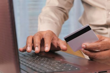 Adamın elleri kredi kartını tutuyor ve internetten bilgisayar alışverişi yapıyor. 