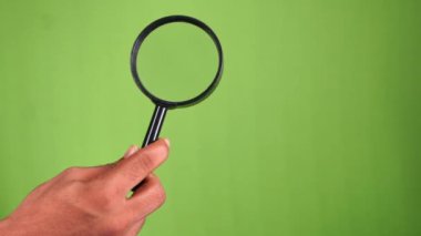 Yeşil ekranda büyüteç tutan el. 