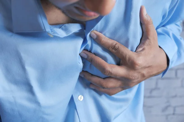 Jonge man lijden pijn in het hart en houden borst met de hand — Stockfoto