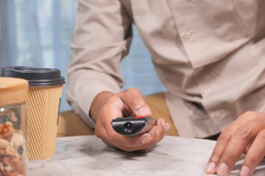 Genç adam televizyon kumandası kullanarak kanepede oturuyor. 